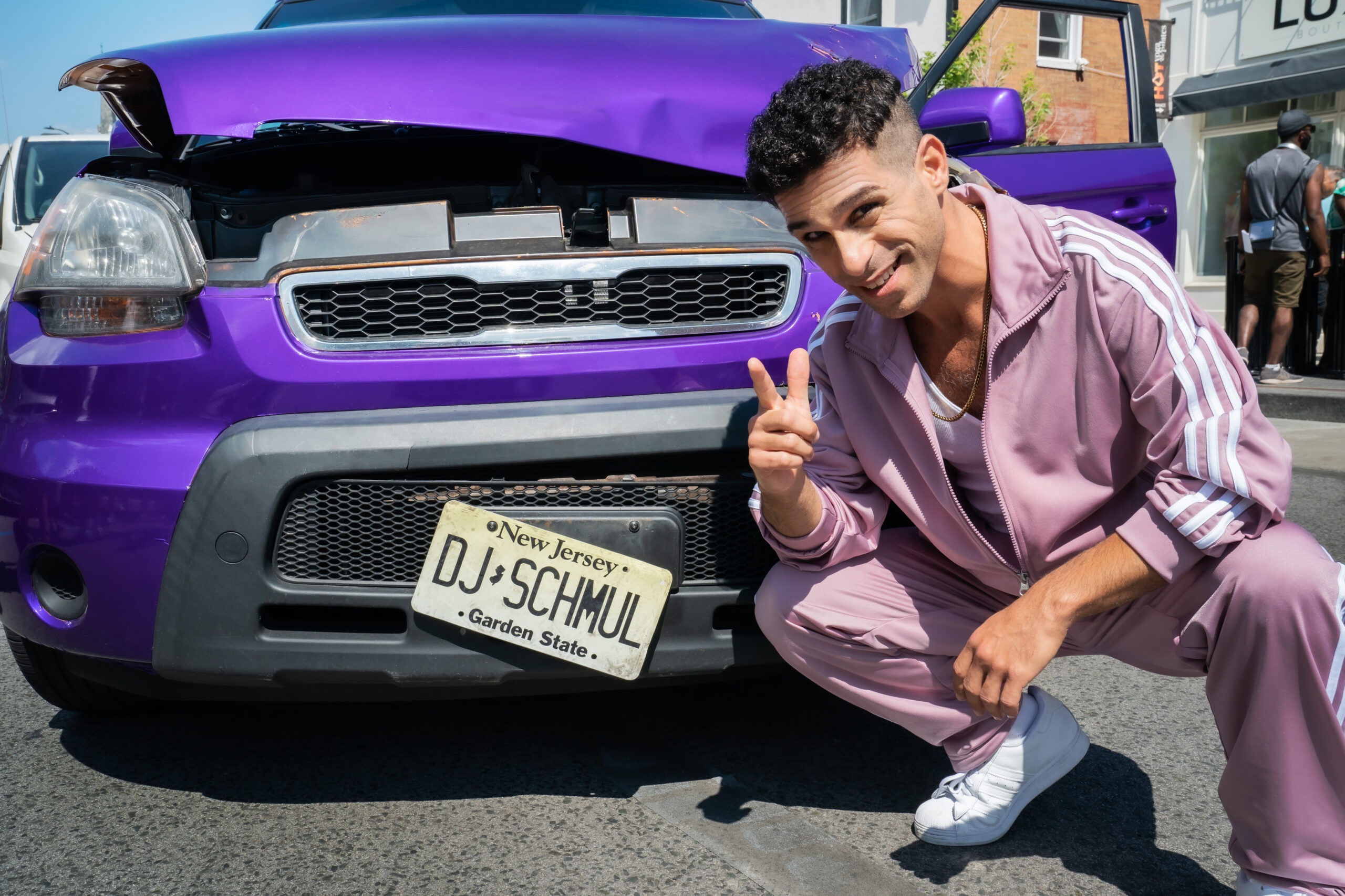 Dj Shmuley in front of a broken down purple car with New Jersey license plates