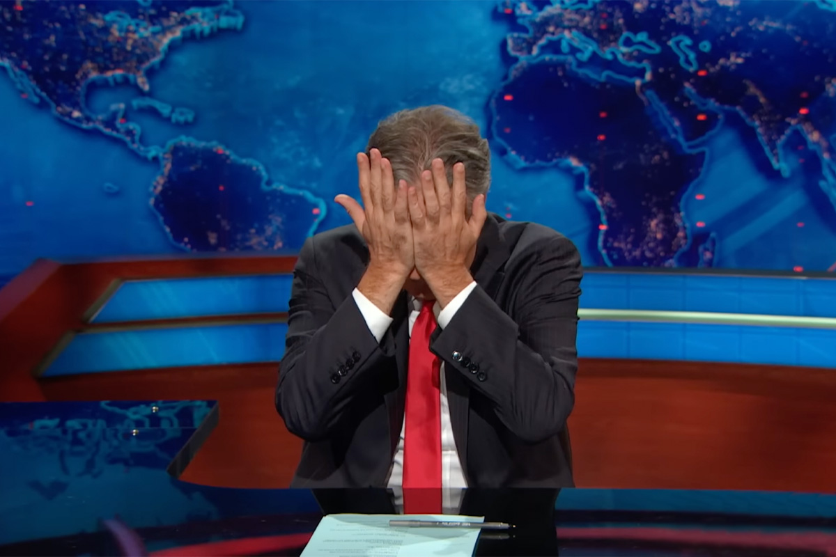 Jon Stewart at a desk with his head in his hands