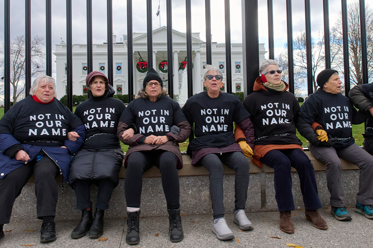6 Jewis elders wearing black t-shirts reading "Not in Our Name" are chained to the fence in front of the White House