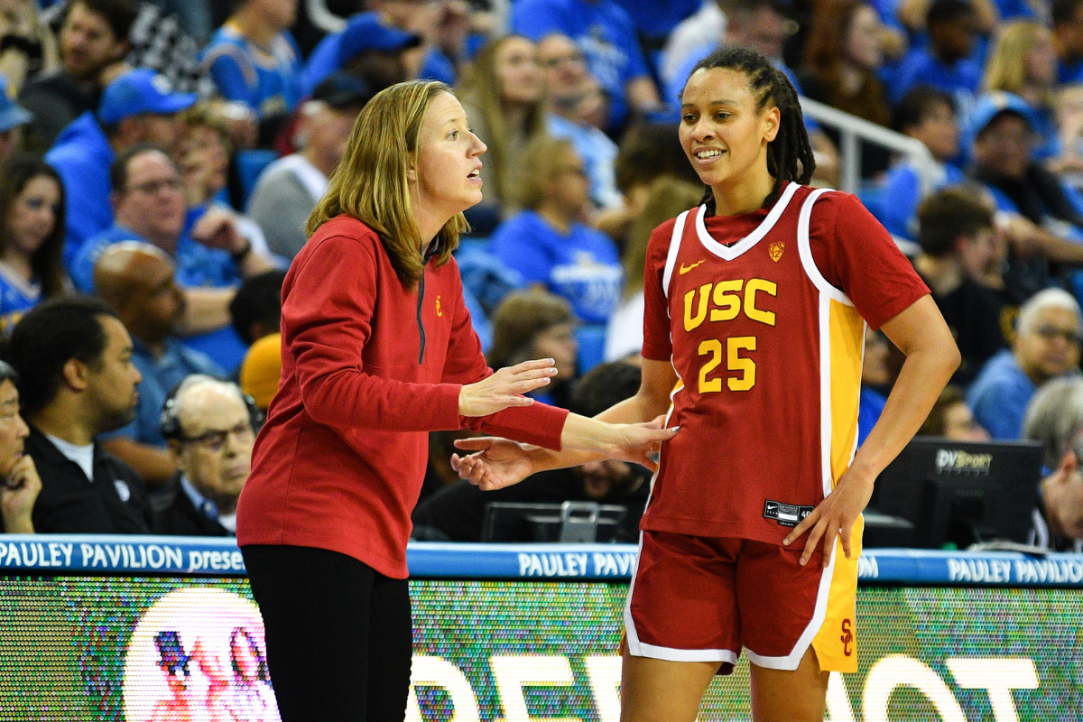 Lindsay Gottlieb, wearing a red long sleeve shirt and black pants, coaches one of her players.