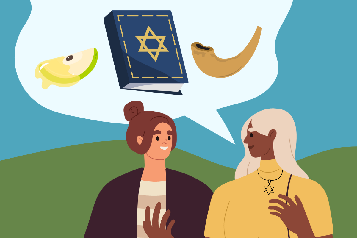 A cartoon depiction of an interfaith couple. The woman on the right has a speech bubble depicting Jewish symbols: an apple dipped in honey, a prayer book, and a shofar. The woman on the left is smiling and listening.