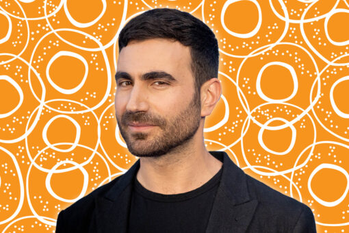 Brett Goldstein stares at camera. Behind him is an orange bagel pattern.