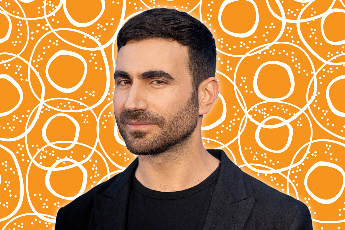 Brett Goldstein stares at camera. Behind him is an orange bagel pattern.