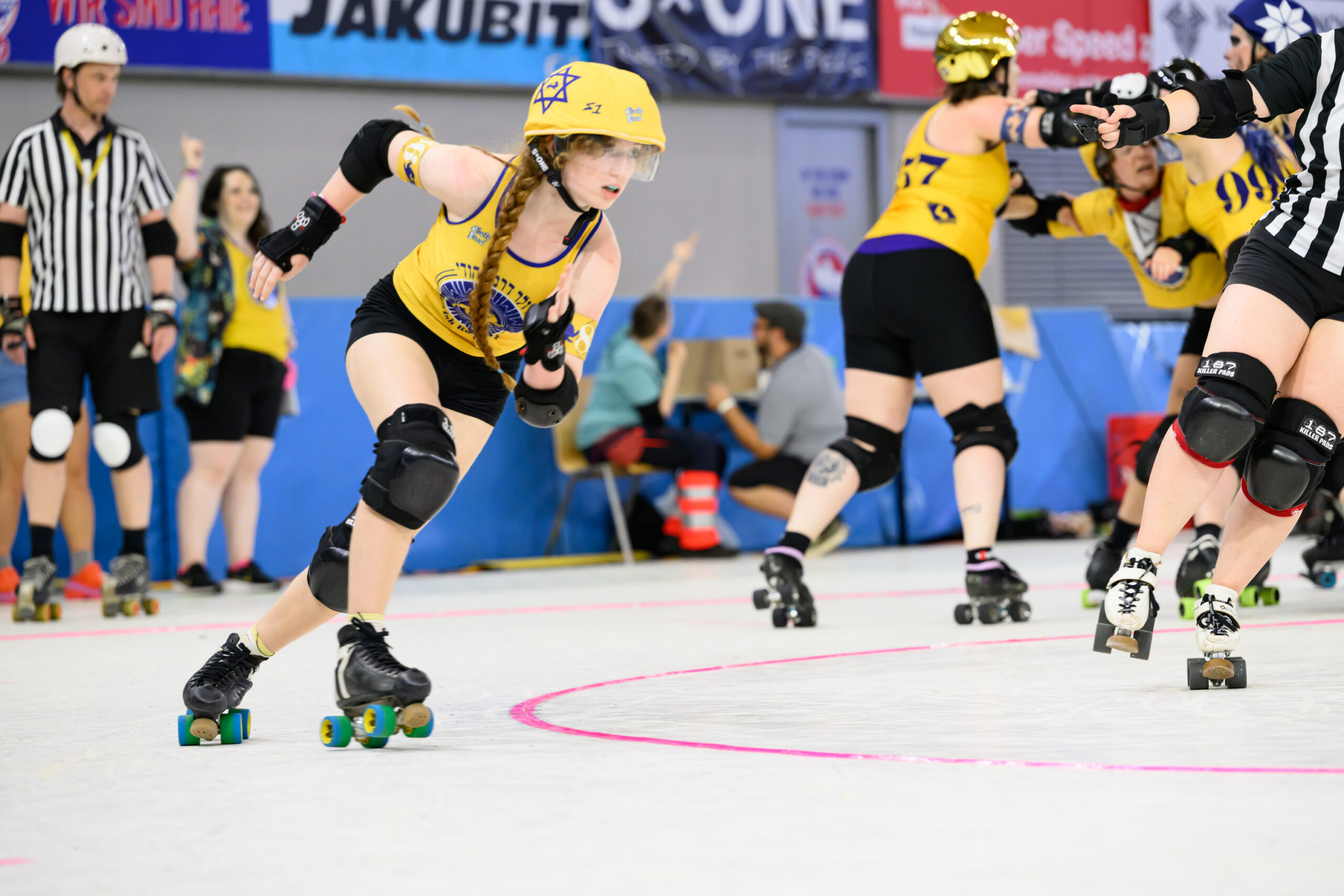 A Jewish Roller Derby skater in yellow breaks away from the pack at the 2025 Roller Derby World Cup.